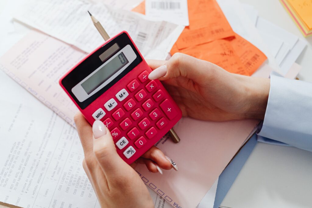 Hands holding a red calculator over bills and documents for calculating Massachusetts paycheck 2026